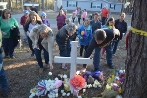Mourners place flowers at the foot of cross in the front of the Alford&#039;s yard.
