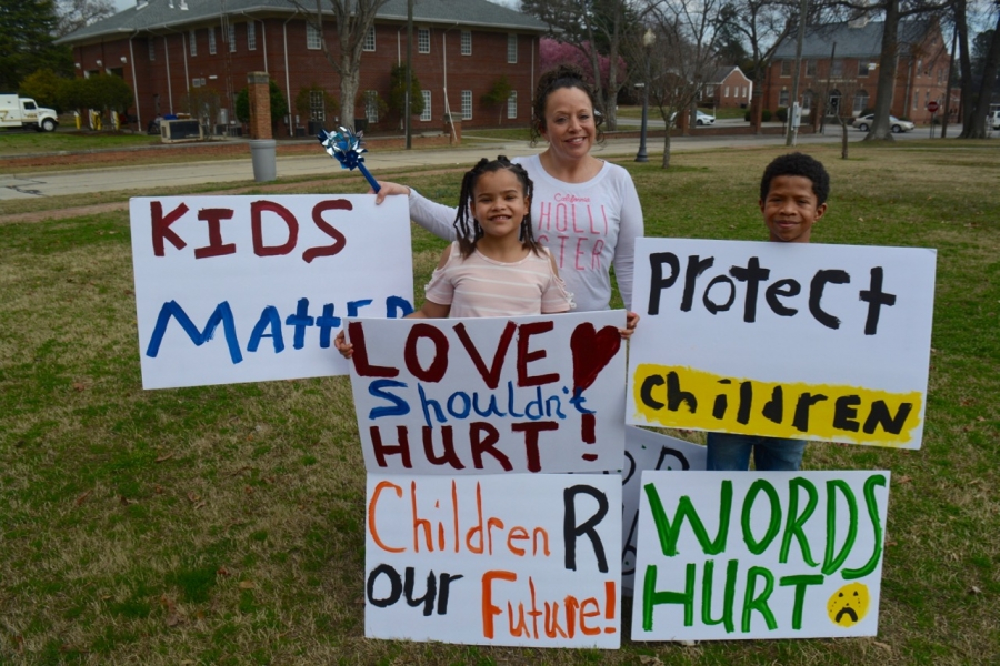 Elijah, his sister, Trinity, and his mother, Jessica, hold signs and pinwheels which will be part of the march.